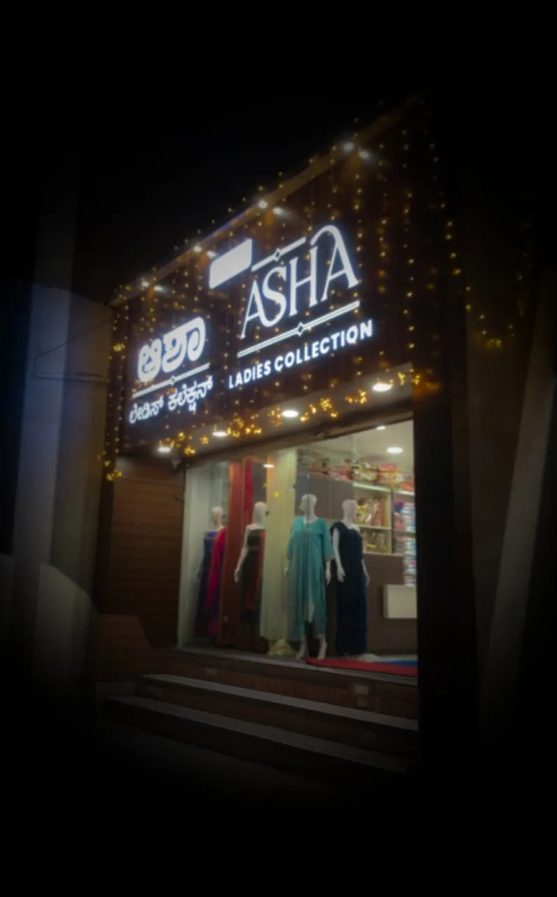 The ASHA Ladies Collection shop front at night, its signboard lit and the windows dressed with mannequins